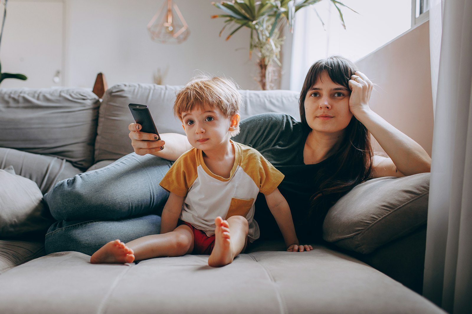 A woman and a child sitting on a couch looking at a phone