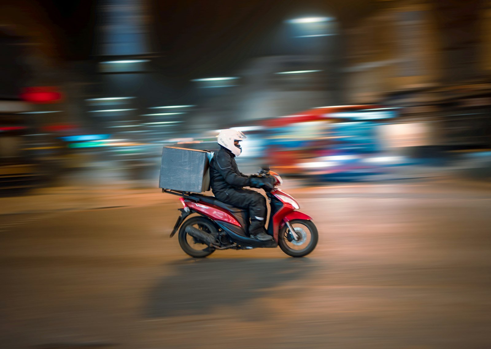A delivery driver on a red scooter riding through a city
